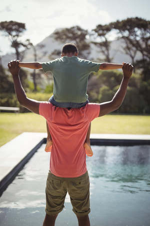 Rear view of father carrying son on shoulders near poolsideの写真素材