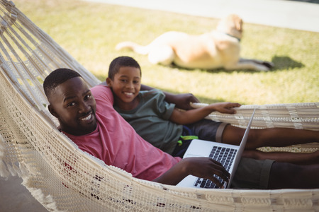 Happy father and son using laptop while relaxing on a hammockの写真素材