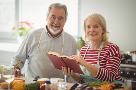 Portrait of smiling senior couple with recipe book standing in kitchenの写真素材