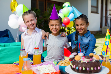 Portrait of children sitting at table during birthday party in yard