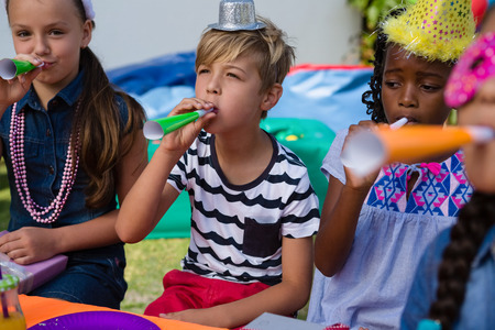 Children blowing part horns during birthday in yardの写真素材