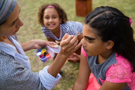 Woman doing face paint to girl during birthday partyの写真素材