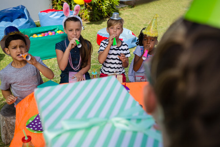 Children blowing party horn during birthday in yard
