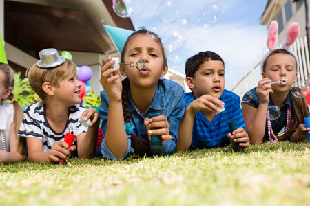 Children blowing bubbles while lying on field in yardの写真素材