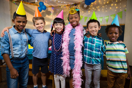Portrait of smiling friends with arm around standing against wall during birthday partyの写真素材