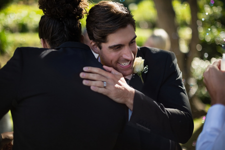 Groom embracing his friend in park during weddingの写真素材