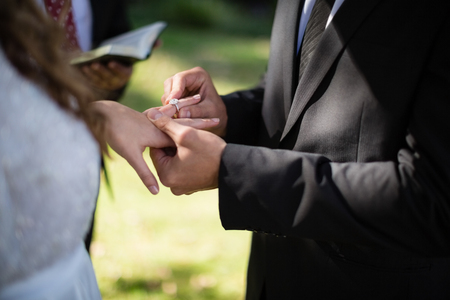 Mid section of groom putting engagement ring in woman fingerの写真素材