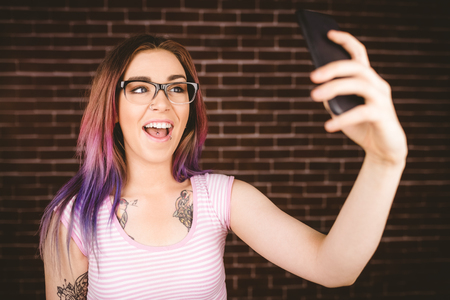Smiling woman taking selfie from mobile phone against brick wallの写真素材