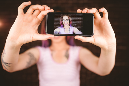 Smiling woman taking selfie from mobile phone against brick wallの写真素材