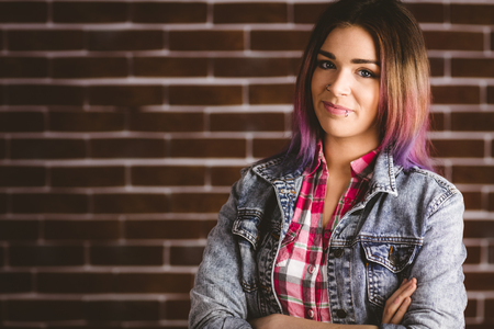 Portrait of smiling woman standing with arms crossed against brick wallの写真素材