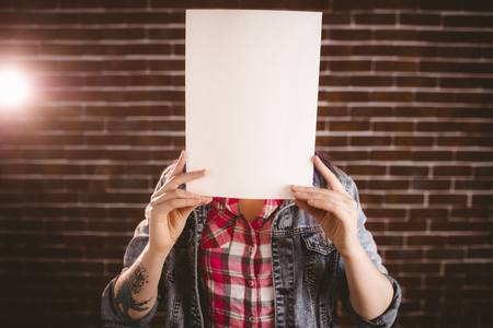 Woman hiding face from blank sheet against brick wallの写真素材
