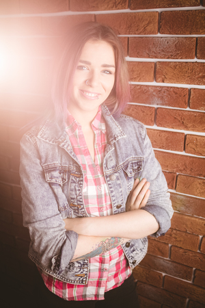 Portrait of smiling woman standing with arms crossed against brick wallの写真素材
