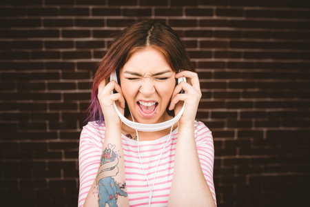 Woman listening music on headphones against brick wallの写真素材