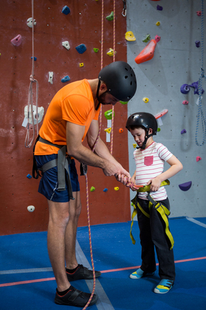 Trainer assisting boy to wear safety harness in fitness studioの写真素材