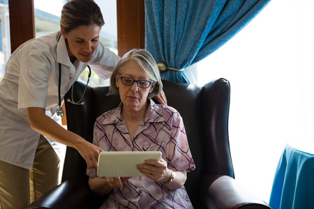 Female doctor assisting woman in using digital tablet at retirement homeの写真素材