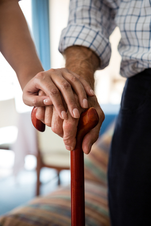 Cropped hands of female doctor and senior man holding walking cane in retirement homeの写真素材