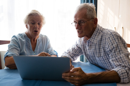 Senior man showing laptop to female friend at table in nursing home