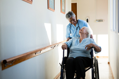 Nurse talking while pushing patient sitting in wheelchair at nursing home