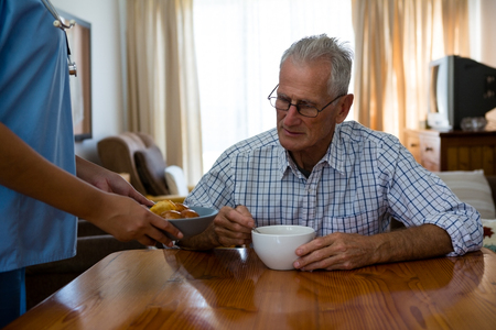 Midsection of female doctor serving food to senior man in nursing homeの写真素材