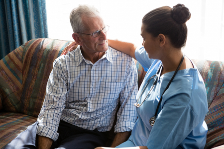 Side view of female doctor consoling senior man while sitting on sofaの写真素材
