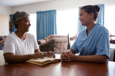 Nurse talking to senior woman while sitting at table in nursing homeの写真素材