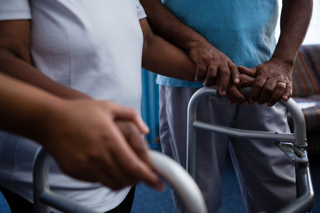 Midsection of friend assisting woman in walking with walker at retirement homeの写真素材