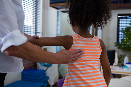 Mid-section of physiotherapist giving back massage to girl patient in clinicの写真素材