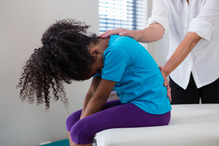 Mid-section of physiotherapist giving back massage to girl patient in clinicの写真素材
