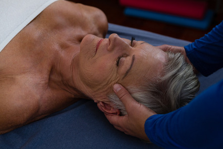 Physiotherapist giving head massage to a senior woman in clinicの写真素材