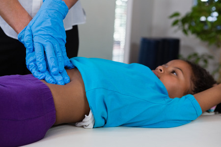 Physiotherapist giving abdomen massage to girl patient in clinicの写真素材