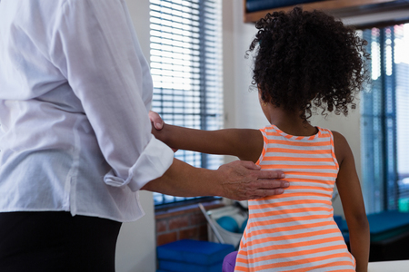 Mid-section of physiotherapist giving back massage to girl patient in clinicの写真素材