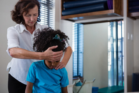 Physiotherapist giving neck massage to girl patient in clinicの写真素材