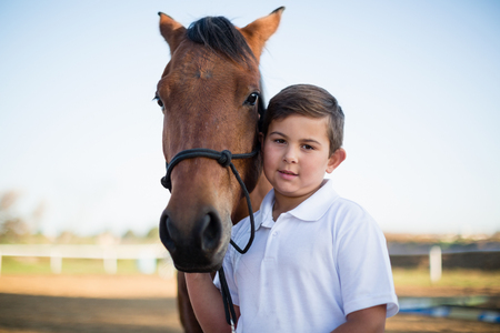 Rider boy caressing a horse in the ranch on a sunny dayの写真素材