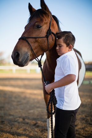 Rider boy caressing a horse in the ranch on a sunny dayの写真素材