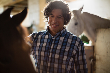 Smiling man caressing the brown horse in the stableの写真素材