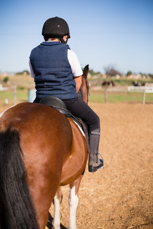 Rear-view of boy riding a horse in the ranchの写真素材