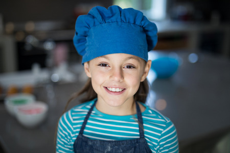 Close-up of smiling girl wearing an apron and a cap in the kitchenの写真素材