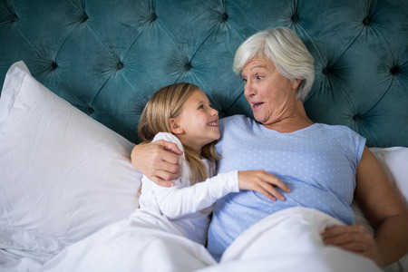 Smiling grandmother and granddaughter interacting with each other on bedの写真素材