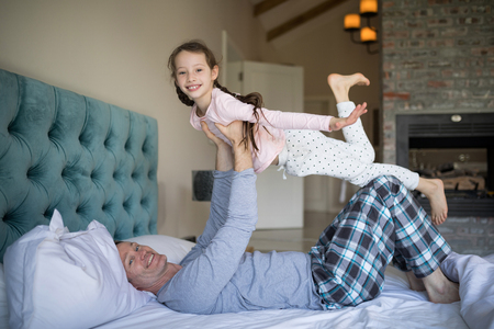 Portrait of happy father and daughter having fun on bed in bedroom at homeの写真素材
