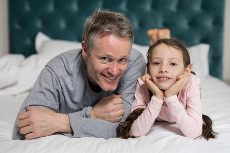 Portrait of smiling father and daughter lying on bed in bedroomの写真素材
