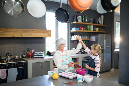 Smiling grandmother and granddaughter giving a high five while making cupcakes in the kitchenの写真素材