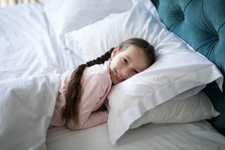 Portrait of smiling girl lying on bed in bedroomの写真素材