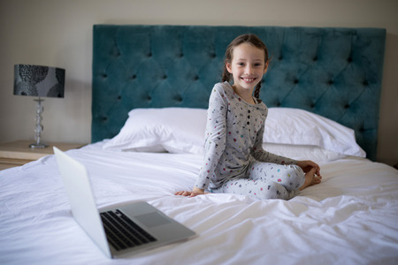 Portrait of smiling girl sitting on bed in bedroomの写真素材