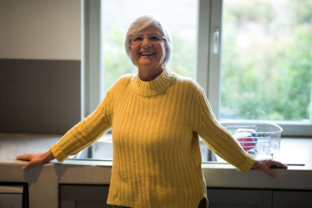 Portrait of smiling senior woman standing near kitchen worktopの写真素材