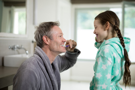 Smiling father and daughter brushing teeth in bathroom at homeの写真素材