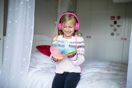 Little girl playing with spring toy with headphones in bedroomの写真素材