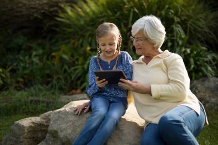 Smiling granddaughter and grandmother using digital tablet in garden on a sunny dayの写真素材