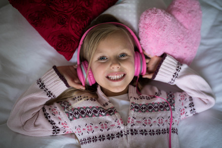 Smiling girl listening to music on headphones while lying on bedの写真素材