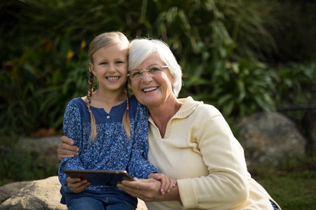Smiling granddaughter and grandmother using digital tablet in garden on a sunny dayの写真素材