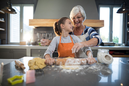 Grandmother helping granddaughter to flatten dough in the kitchenの写真素材
